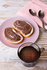 Spread chocolate-nut cream on slices of bread with a Cup of tea. Delicious Breakfast with chocolate and nut paste and a Cup of tea.