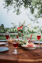 Dinner in an apple orchard garden on wooden table with salads and wine decorated with flowers. Close up of table with food prepared for family dinner