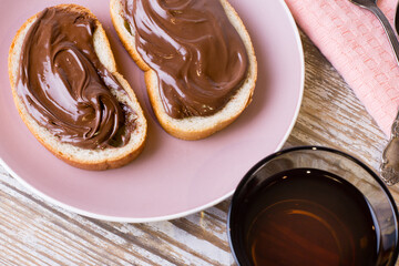 Spread chocolate-nut cream on slices of bread with a Cup of tea. Delicious Breakfast with chocolate and nut paste and a Cup of tea.