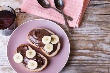 Chocolate-nut cream with banana on slices of bread with a Cup of tea. Delicious Breakfast with chocolate and nut paste with banana and a Cup of tea. Copy space.