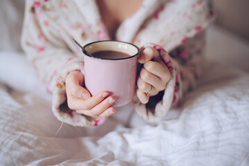 Closeup of female hands holding a cup with tea in the bed