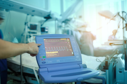 Heart Monitoring Device At The Patient In The ER Surrounded By Working Medical Staff And Operating Surgical Team