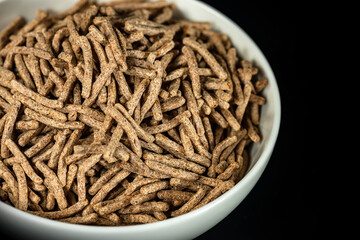Extreme close-up of a white cup full of sticks of bran isolated on black background.