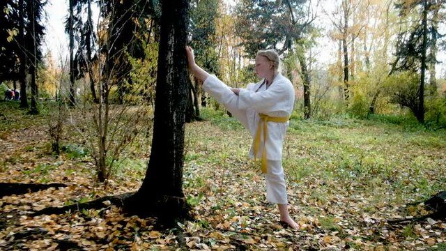teenager girl 12 years old is engaged in karate outdoors in the park. Healthy lifestyle concept. playing sports. martial arts. Judo, Jiujitsu. bold, strong, stretches the legs by the tree. Workouts