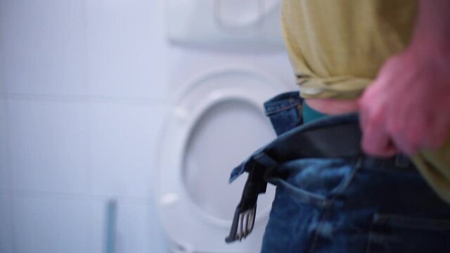 A man in a public toilet zips his pants and belt after bowel movement. Body service in the restroom.