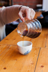 female barista pours black coffee into a ceramic cup from a glass server decanter. coffee shop...