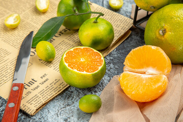 Top view of fresh citrus fruits with leaves cut in half forms and knife on newspaper on gray background