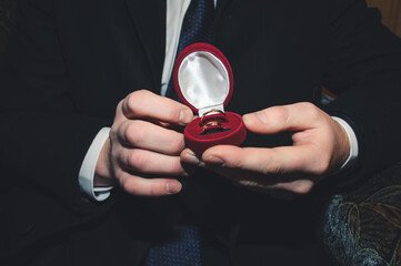 two gold wedding rings lie in a red box on the male hand
