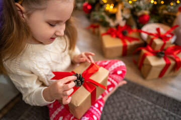 Fototapeta na wymiar Happy smiling baby girl with deer antlers holds a gift box near Christmas tree