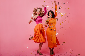 Obraz na płótnie Canvas Curly blonde woman jumping on pink background. Studio portrait of two shapely girls dancing with smile.