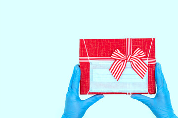 Red gift box with wearing a protective medical mask on a pastel background, copy space. The concept of safe gifts for the New Year 2021, Christmas, Valentine's Day