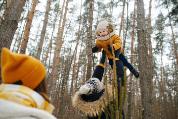 Dad lifting his happy little daughter up in the air during family stroll in a winter conifer...
