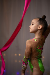 Little girl gymnast in colorful bright leotard dancing with crimson ribbon