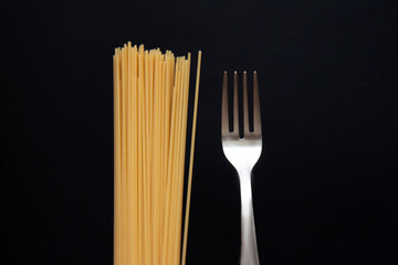 Raw spaghetti with a fork isolated on black background. Pasta. Selective focus