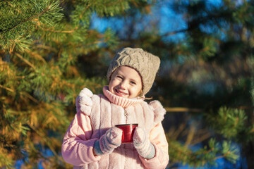 Little girl is Holding a cup with hot tea In Winter forest.