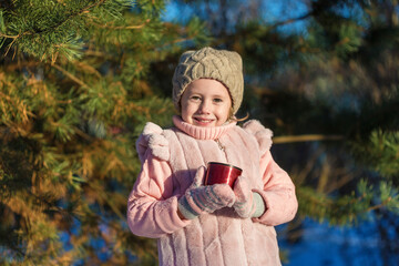 Cute Little girl is Holding a cup with hot tea In Winter forest.