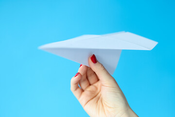 Female hand holding paper plane on blue background