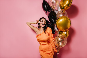 Blissful slim woman dancing at her birthday party. Latin girl in orange dress enjoying event.