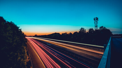 Light streaks shot of motorway with cell tower silhouette	