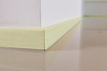 Close-up of a yellow masking painters tape to protect the plinth, before painting the floor or installing a synthetic cast floor.