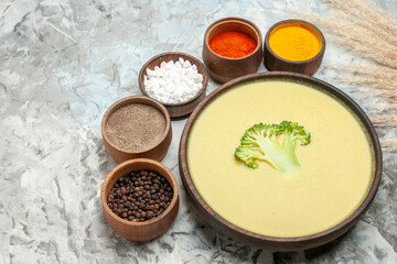 Close up view of creamy broccoli soup in a brown bowl and different spices on gray background