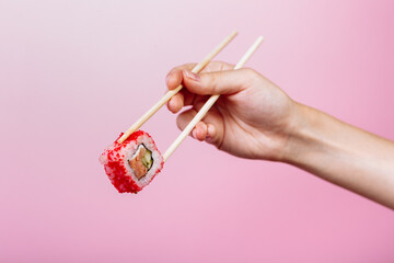 Tasty sushi roll California with wooden chopsticks on pink background close up. Place for caption and text