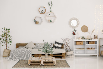 White living room. A sofa made of wooden pallets, green plants in pots, a chest of drawers, a round...