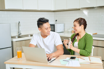 Fototapeta premium Young couple managing finances, reviewing their bank accounts using laptop computer and calculator at modern kitchen.