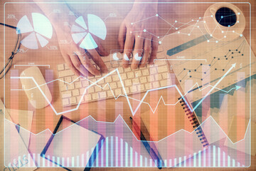 Multi exposure of man's hands typing over computer keyboard and forex graph hologram drawing. Top...