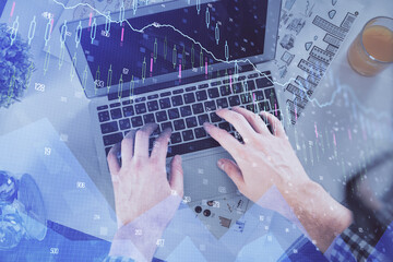 Double exposure of man's hands typing over laptop keyboard and forex chart hologram drawing. Top view. Financial markets concept.