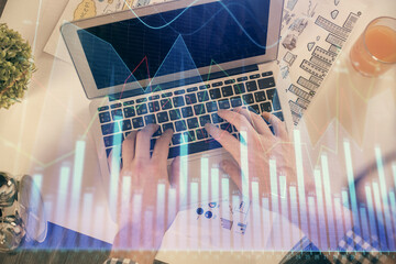Double exposure of man's hands typing over laptop keyboard and forex chart hologram drawing. Top view. Financial markets concept.