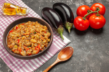 top view roasted eggplant salad in bowl wooden spoon tomatoes eggplants oil bottle on dark background