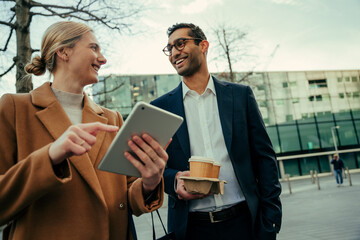 Mixed race business partners smiling while discussing business plans researching on digital tablet walking to work 