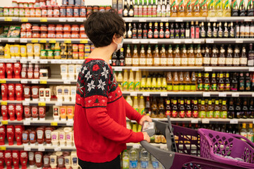 shopping woman wearing medical mask short hair at the grocery store for christmas or new year dinner table. shopping cart, ugly christmas sweater. coronavirus times pandemic. blurry photo. 2021