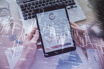 Double exposure of man's hands holding and using a digital device and forex graph drawing. Financial market concept.