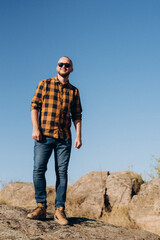 bald guy with a beard in jeans warm shirt and trekking shoes