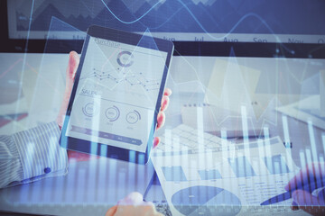 Double exposure of man's hands holding and using a digital device and forex graph drawing. Financial market concept.