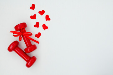 Two red dumbbells and hearts on a white background with copy space. Concept of Valentines day, healthy lifestyle, giving gifts, love of sports, shopping