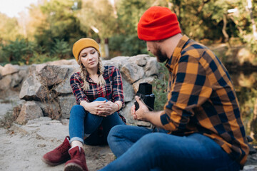 Bald guy with a beard and a blonde girl in bright hats are taking pictures with an old camera