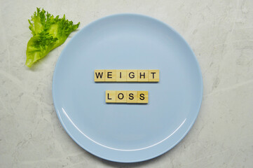 Phrase weight loss made of wooden letters on a blue plate with a leaf of lettuce