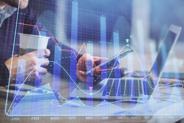 Double exposure of man's hands holding and using a phone and financial graph drawing. Analysis concept.