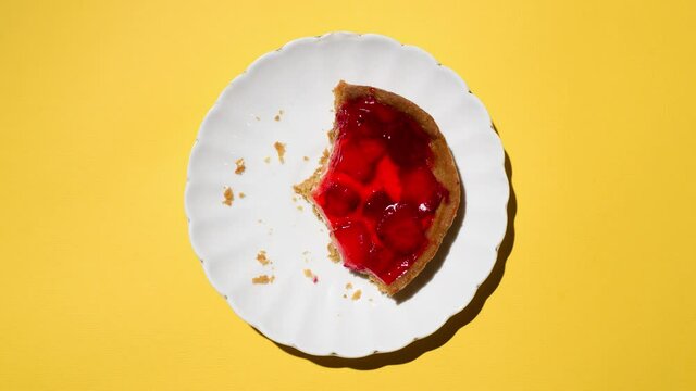 Eating strawberry cheesecake bite by bite, stop motion. Plate of cake moving in the frame. Food animation, top view, light yellow background