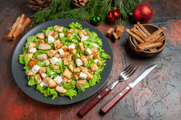 top view caesar salad on oval plate fork knife bowl with dried crust xmas tree toys cinnamon sticks on dark red background