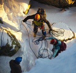 Group of three climbers in snowy couloir prepare rope while climbing in the winter mountains. Taganay National Park, South Ural.