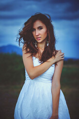 Fototapeta premium A beautiful woman stands in a field.The wind blows the girl's hair.cloudy day.The concept of beauty and ecology.