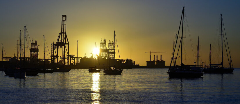 Sunrise from the bay with anchored sailboats in the foreground and commercial port in the background
