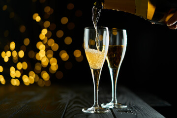 Two glasses of sparkling wine or champagne to celebrate New Year, Merry Christmas, Party or Anniversary with a yellow bokeh effect on dark background. 