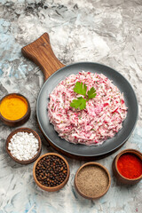 Above view of delicious chicken salad with mayonnaise and beet served with green on brown wooden cutting board and different spices lined up in a row on ice table