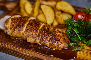 Chicken fillet in sweet and sour sauce with potatoes on a wooden board