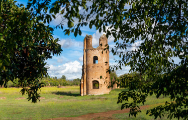 Circus of Maxentius Appia Antica, detail of the brick tower framed among the trees, the clouds, the blue sky and the green lawn. Rome Italy.